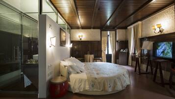 A modern hotel room with a large bed, a glass shower enclosure, and a television.