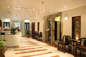 Una hall d'albergo con una reception, un'area salotto e un grande quadro appeso al muro.