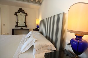 Una camera d'albergo con un letto, una lampada da comodino, uno specchio e una testiera a righe.