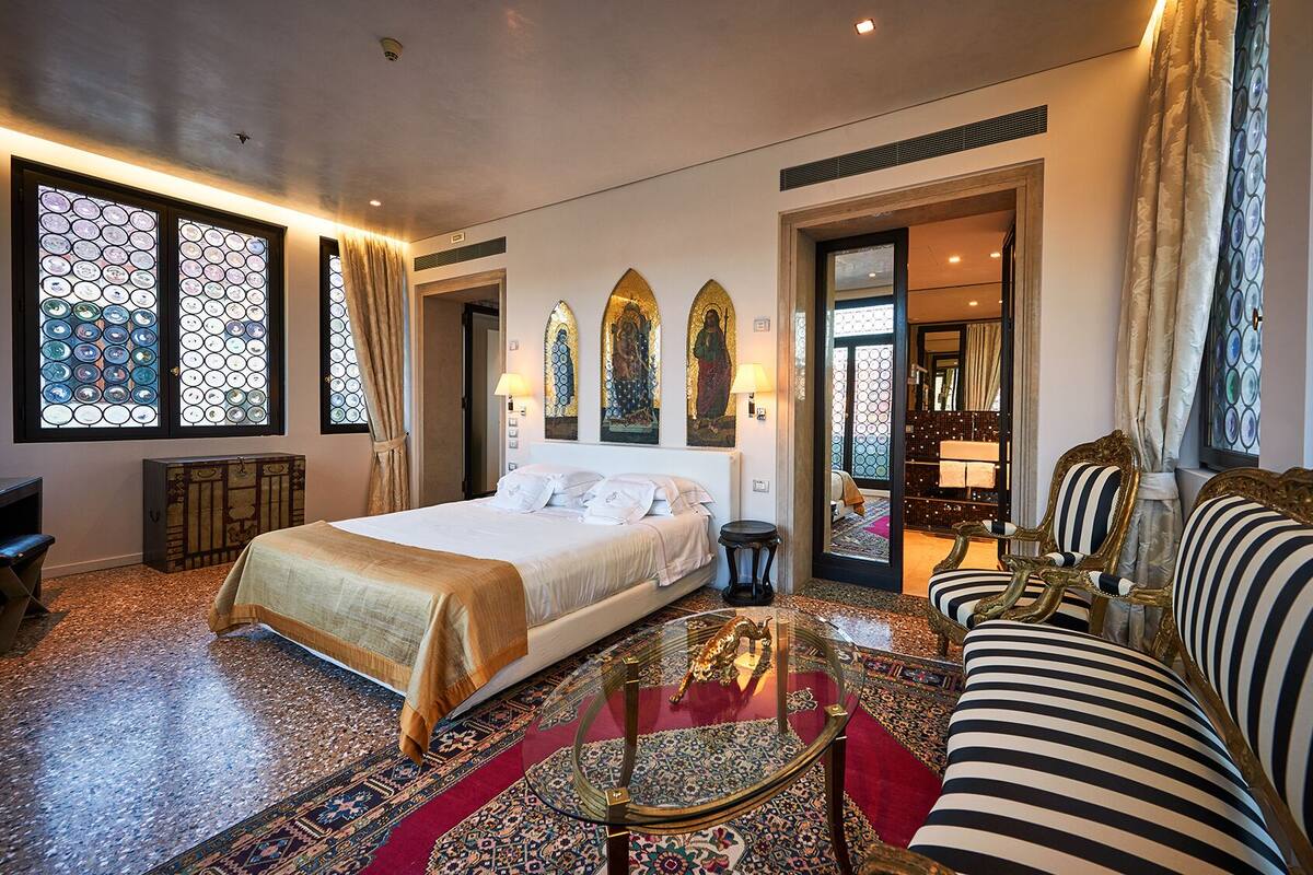 A spacious hotel room with a large bed, a sofa, a glass coffee table, and a view of a bathroom through an open door.