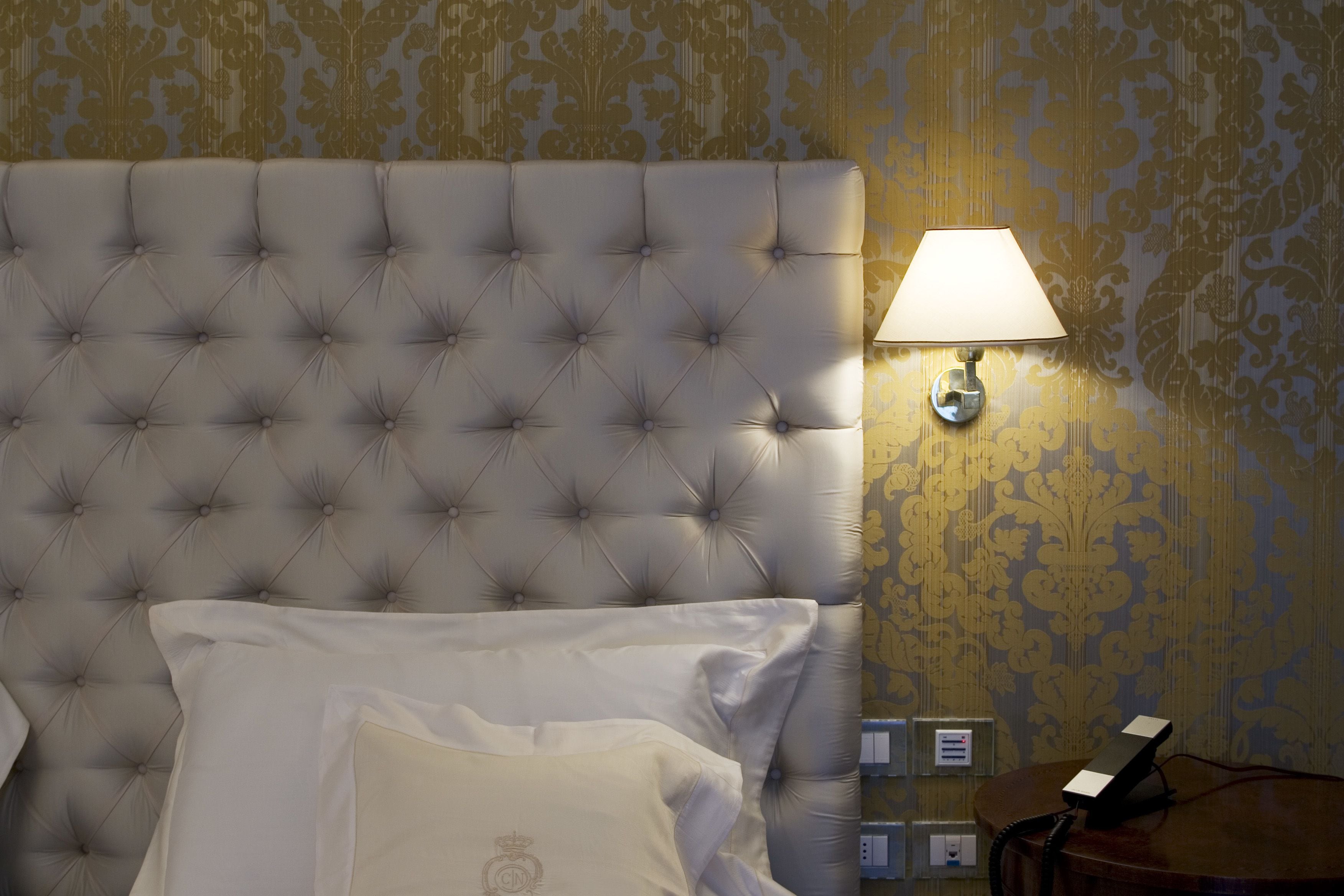 Een slaapkamer met een gestoffeerd hoofdeinde, een bedlamp en een telefoon op een houten nachtkastje.