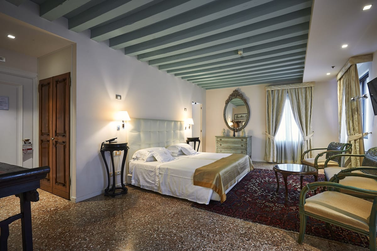A hotel room with a bed, bedside tables, a desk, a chair, a mirror, and a television.