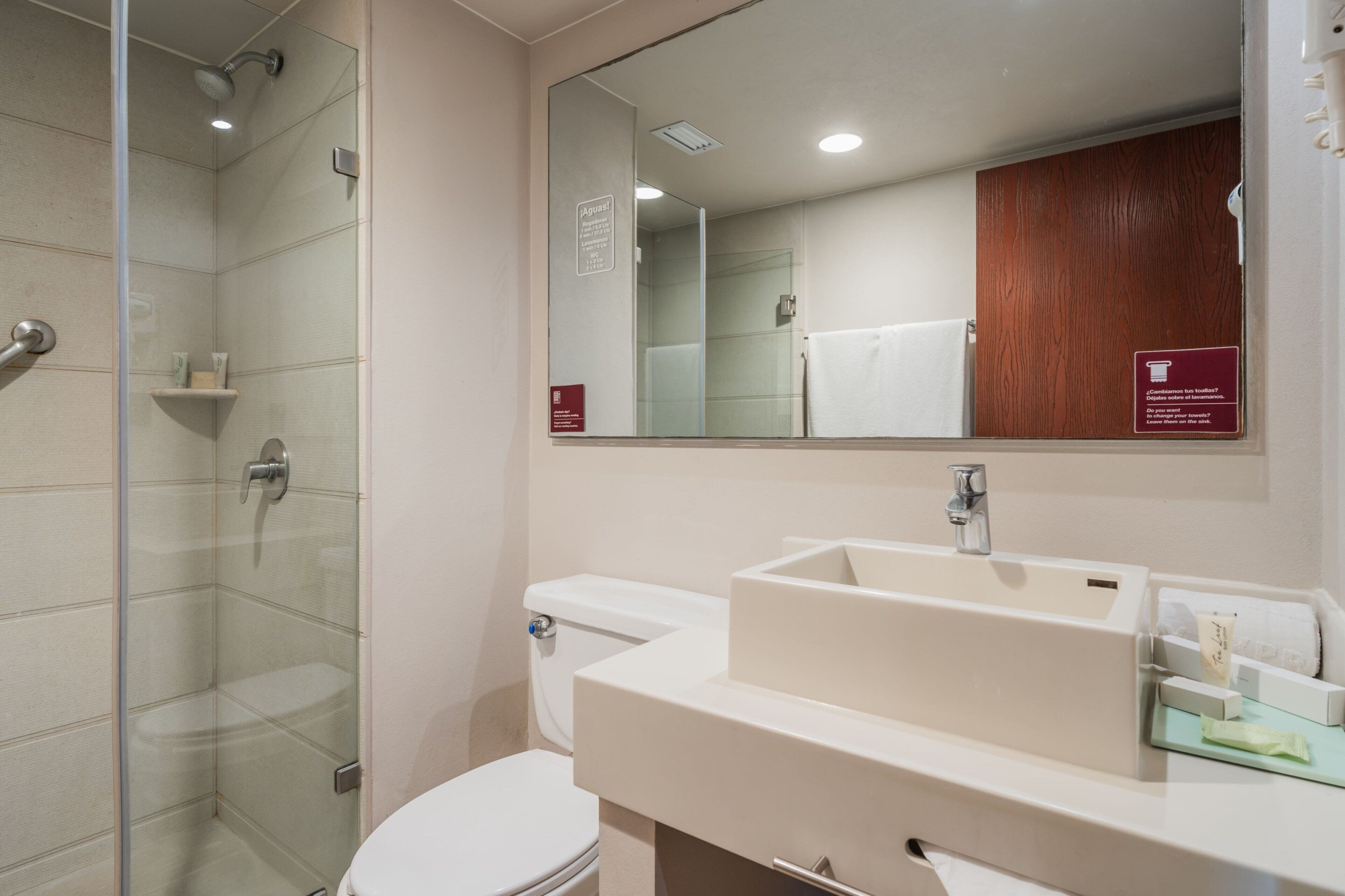 Een moderne badkamer met een douchecabine van glas, een wit toilet en een groot wastafelmeubel met een spiegel erboven.