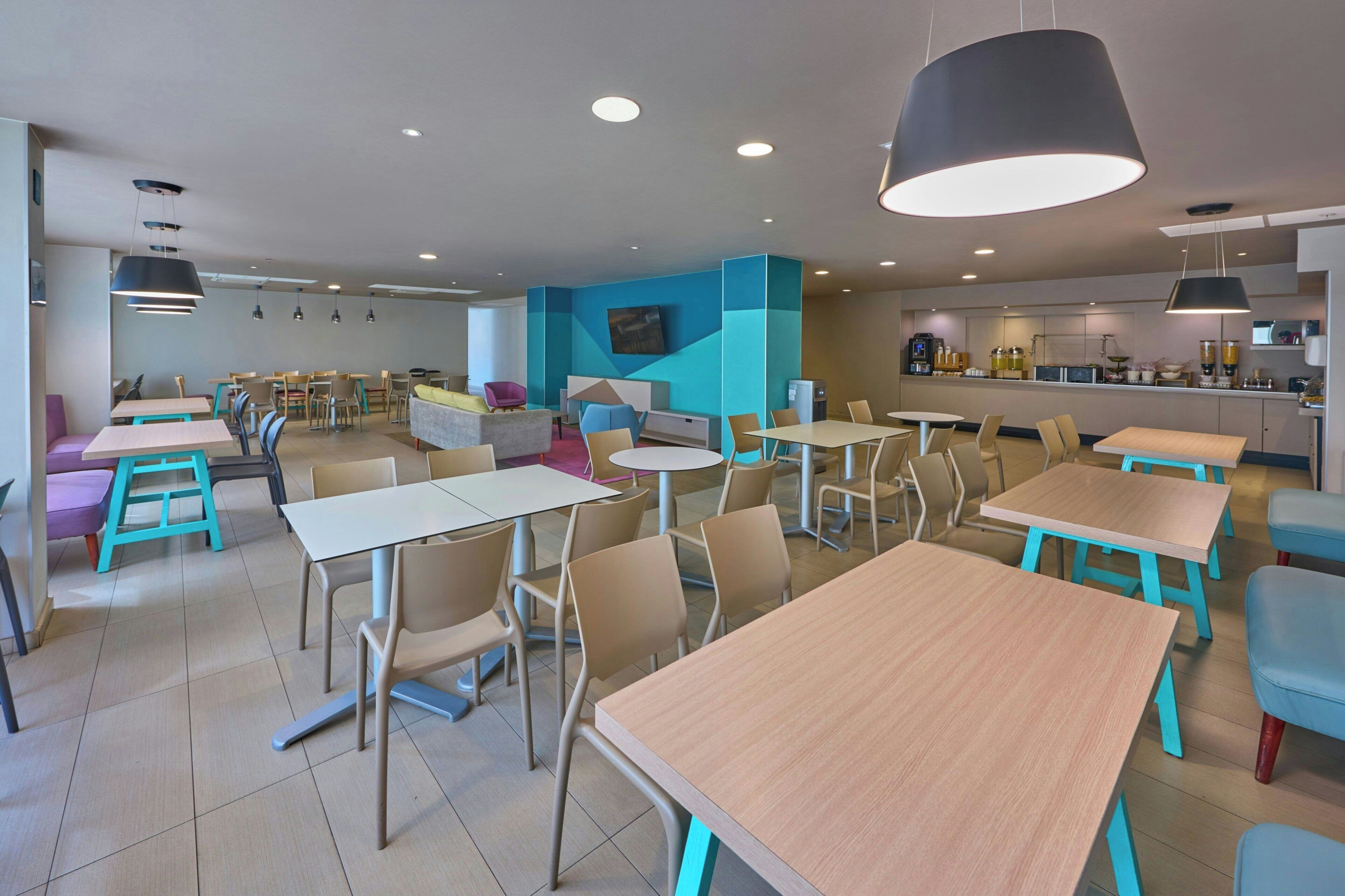 A modern dining area with multiple tables and chairs, a kitchen in the background, and a blue accent wall.