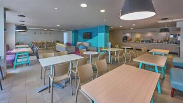 A modern dining area with multiple tables and chairs, a kitchen in the background, and a blue accent wall.