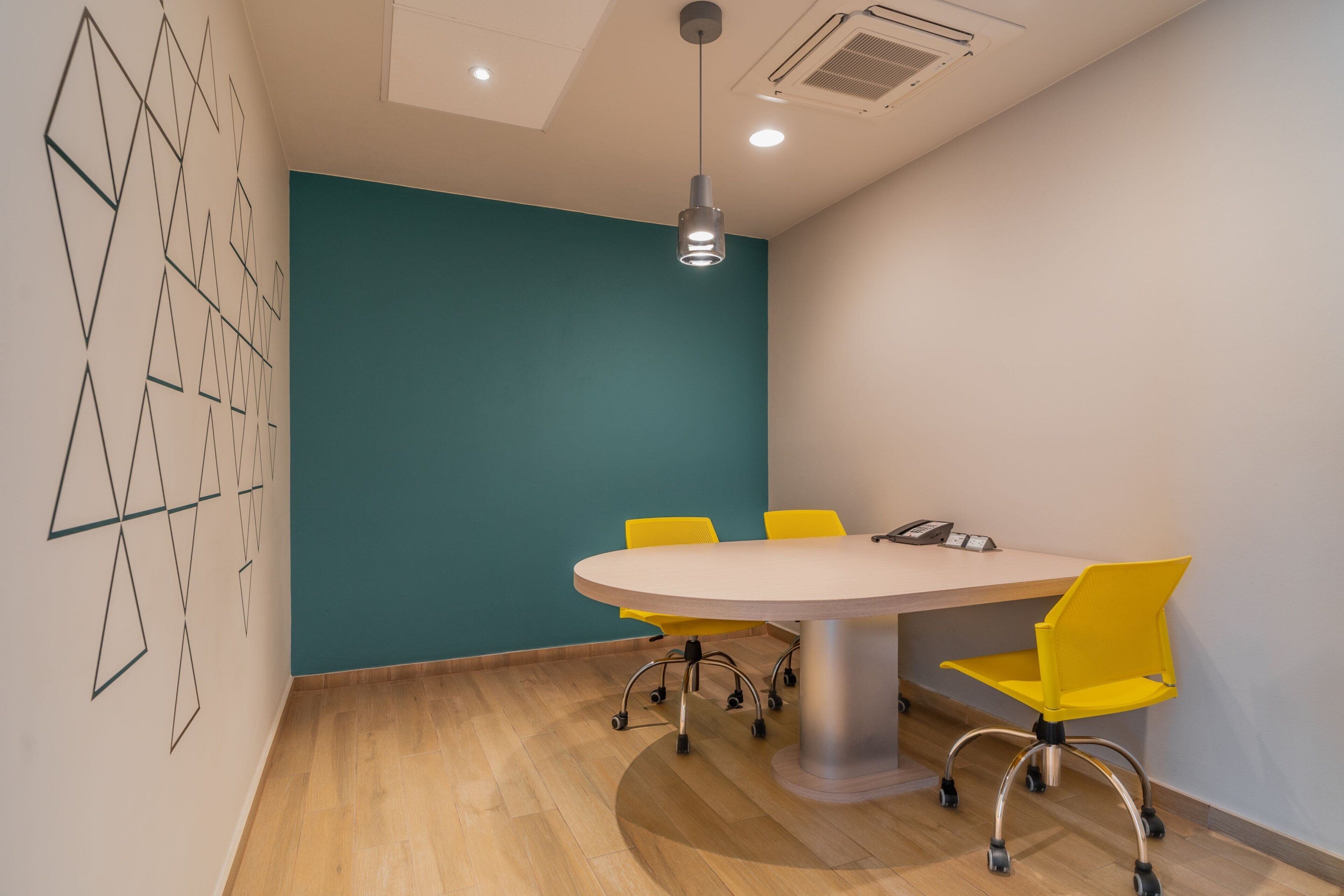 Une salle de conférence avec une table ronde, des chaises jaunes, des murs de couleur turquoise et un luminaire au plafond.