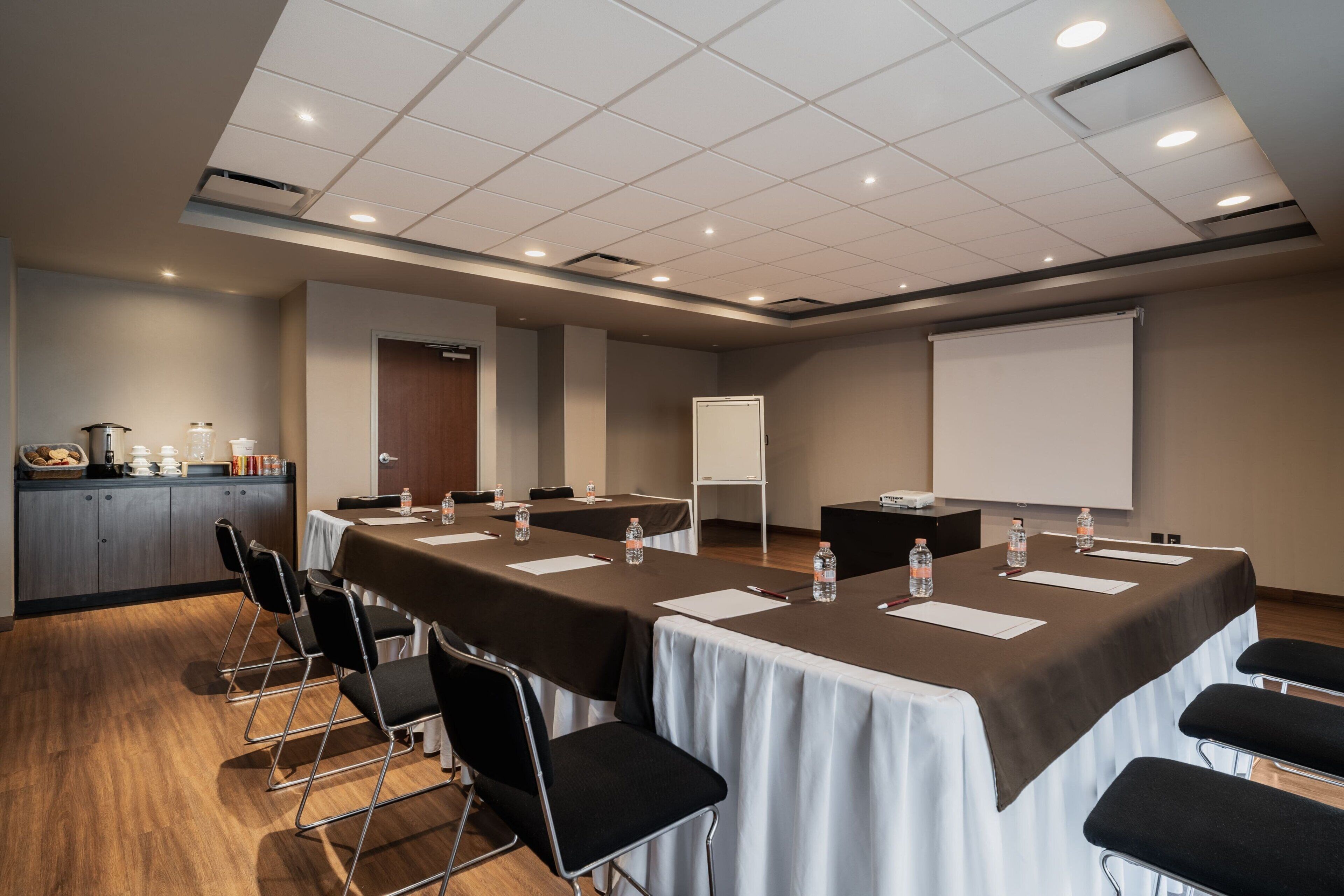 Une salle de conférence équipée d’une longue table, de chaises, d’un écran de projection et d’un tableau blanc.