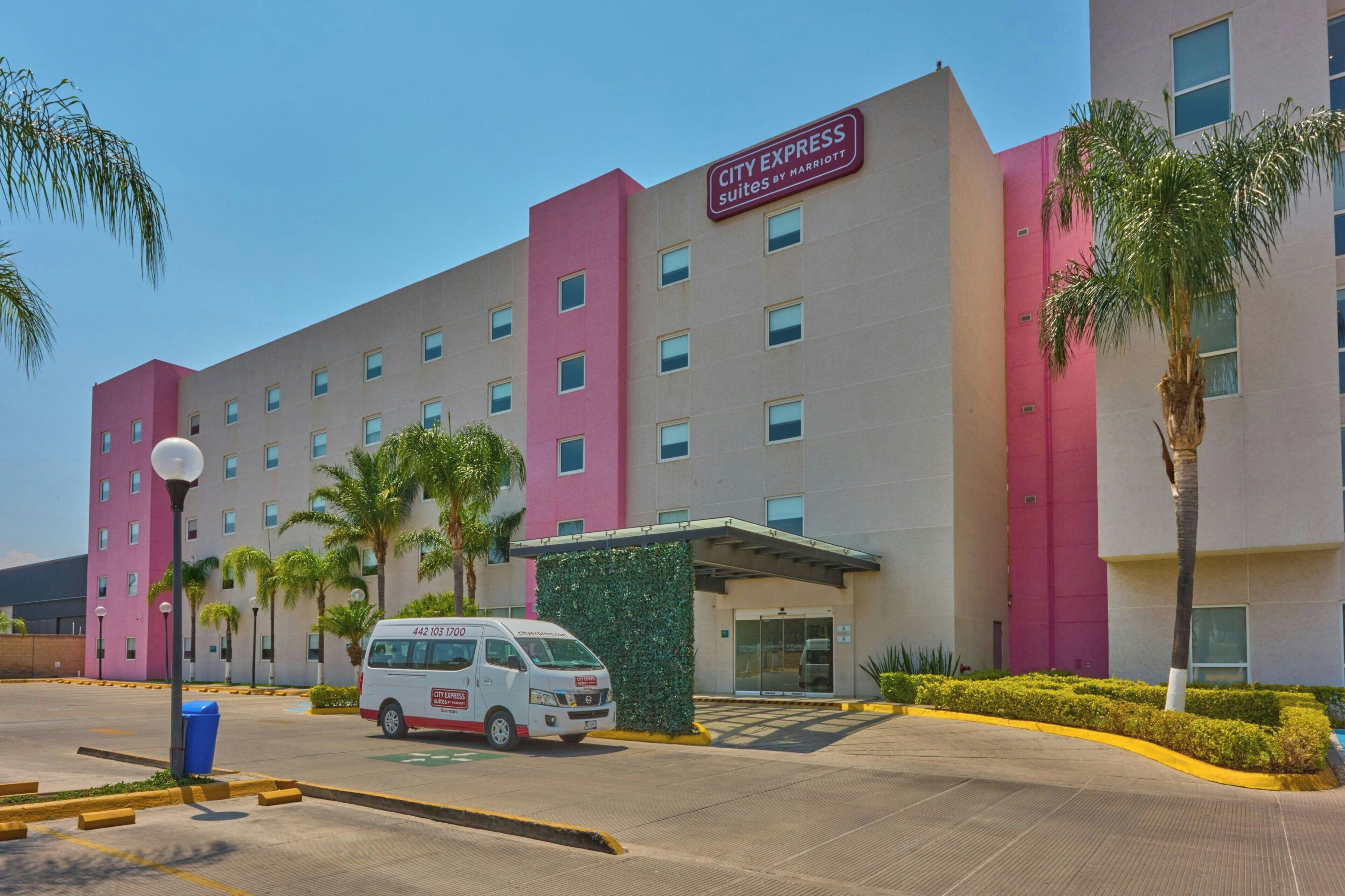 A multi-story hotel with a prominent City Express sign, a parking lot, and palm trees.