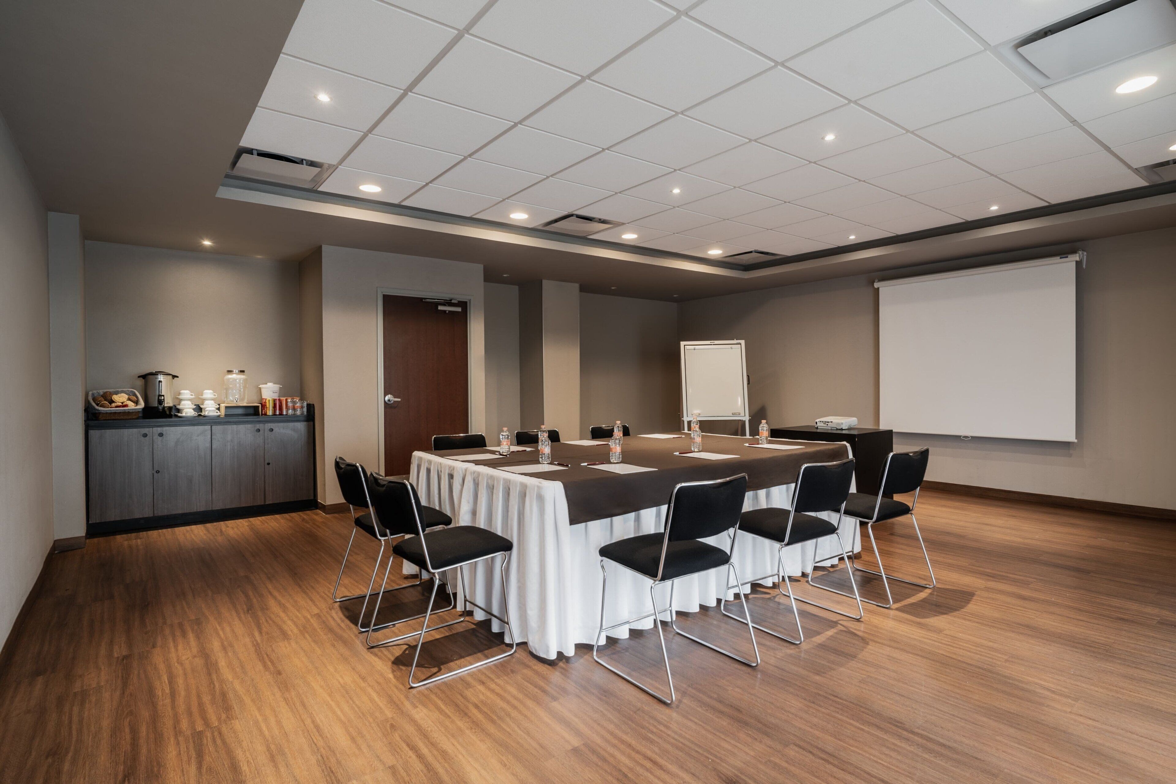 Un salón de conferencias con una larga mesa, sillas, una pantalla de proyector y una pizarra.