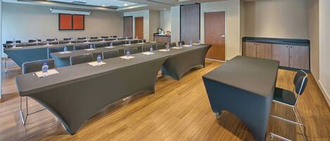 A conference room with long tables, chairs, a podium, and a projection screen.