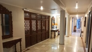 A hallway with a tiled floor, a wooden partition with intricate designs, a mirror, and a table with a lamp. - Hotel Alcala del Rio (Santiago)