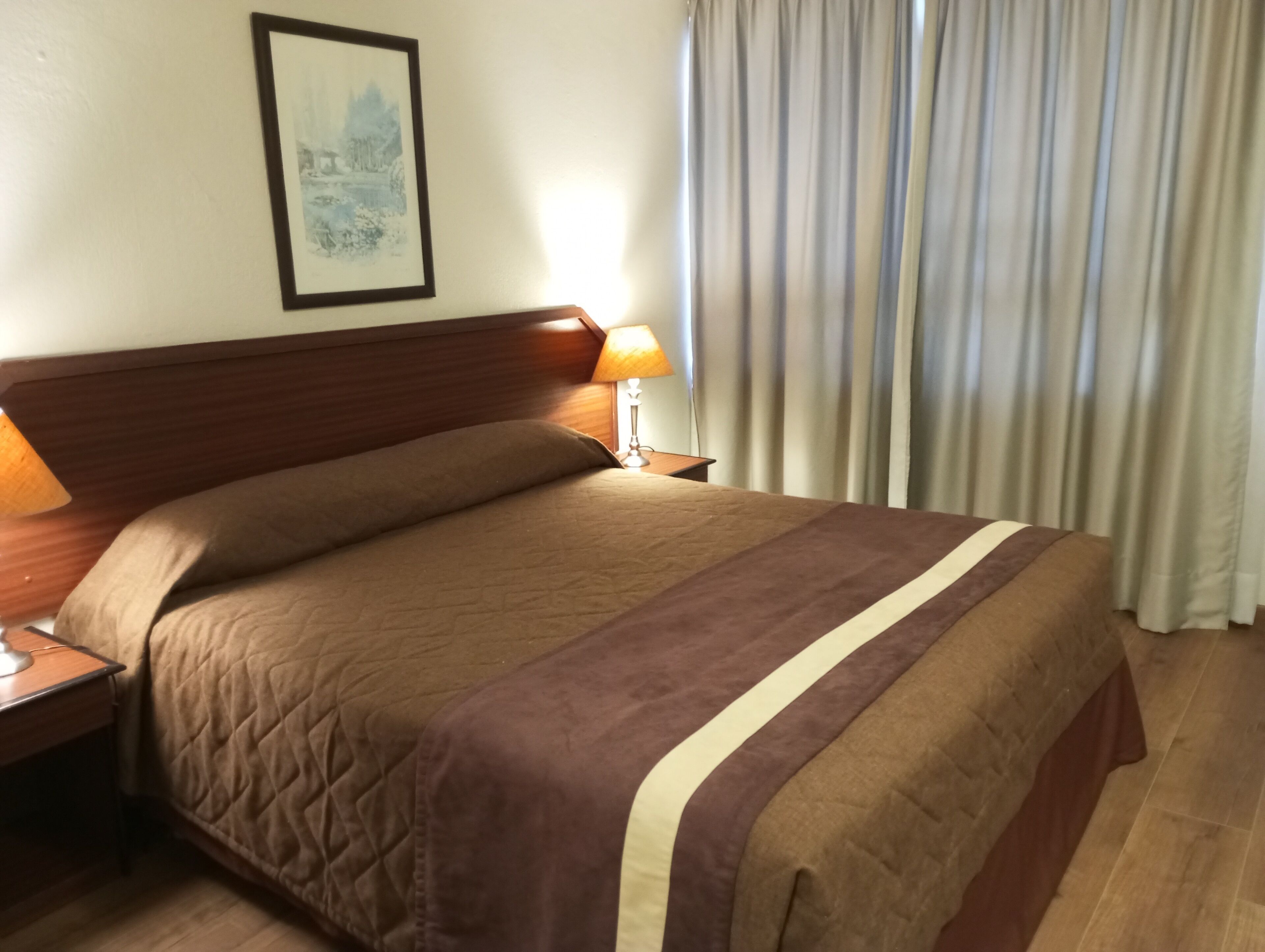 A neatly made bed with a quilted cover, a wooden headboard, and a bedside table with a lamp.