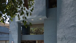A modern building with a blue exterior, a visible number '331', and a paved courtyard with grass. - Hotel Alcala del Rio (Santiago)