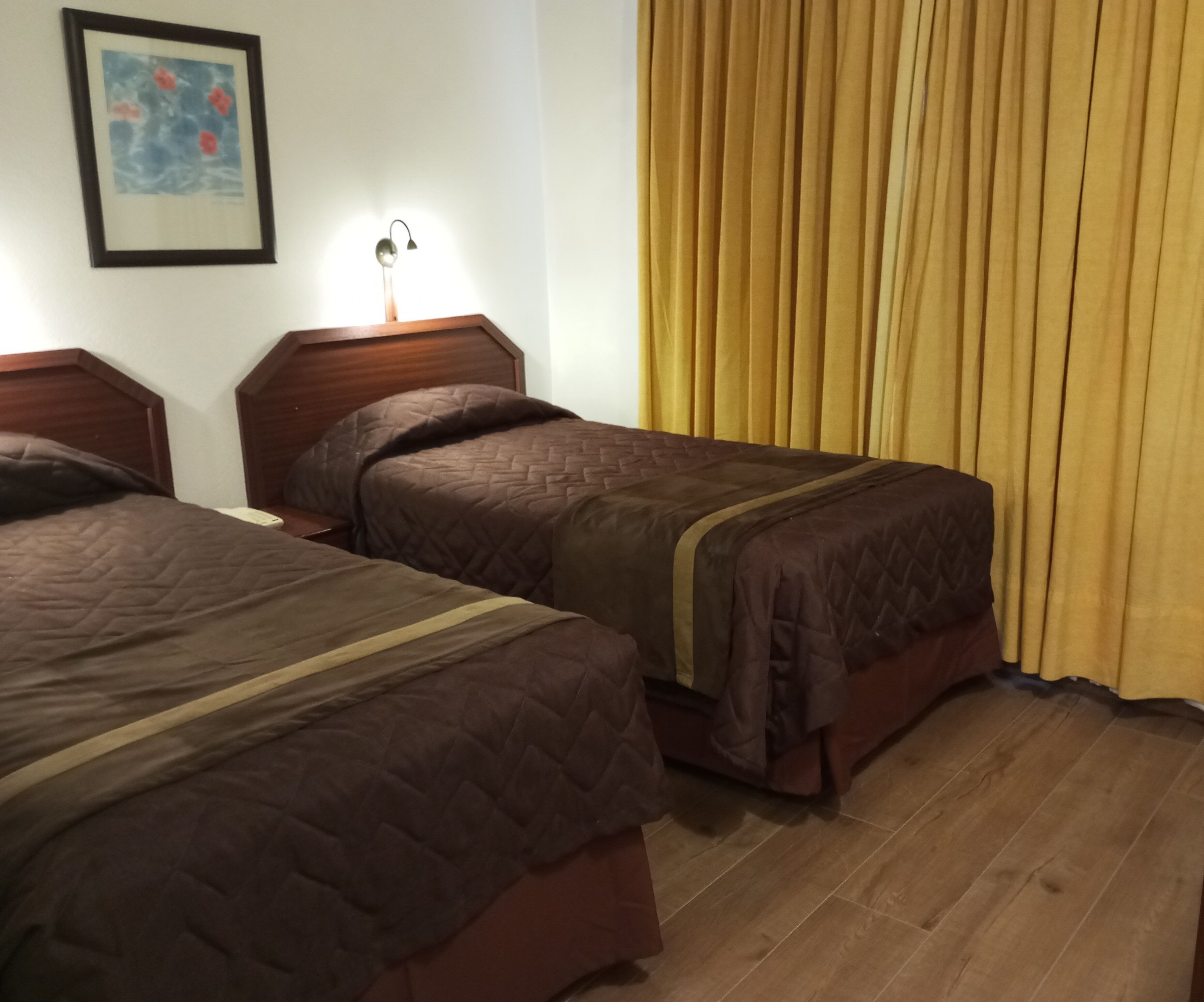 Two single beds with wooden headboards, a bedside table with a lamp, and a yellow curtain.