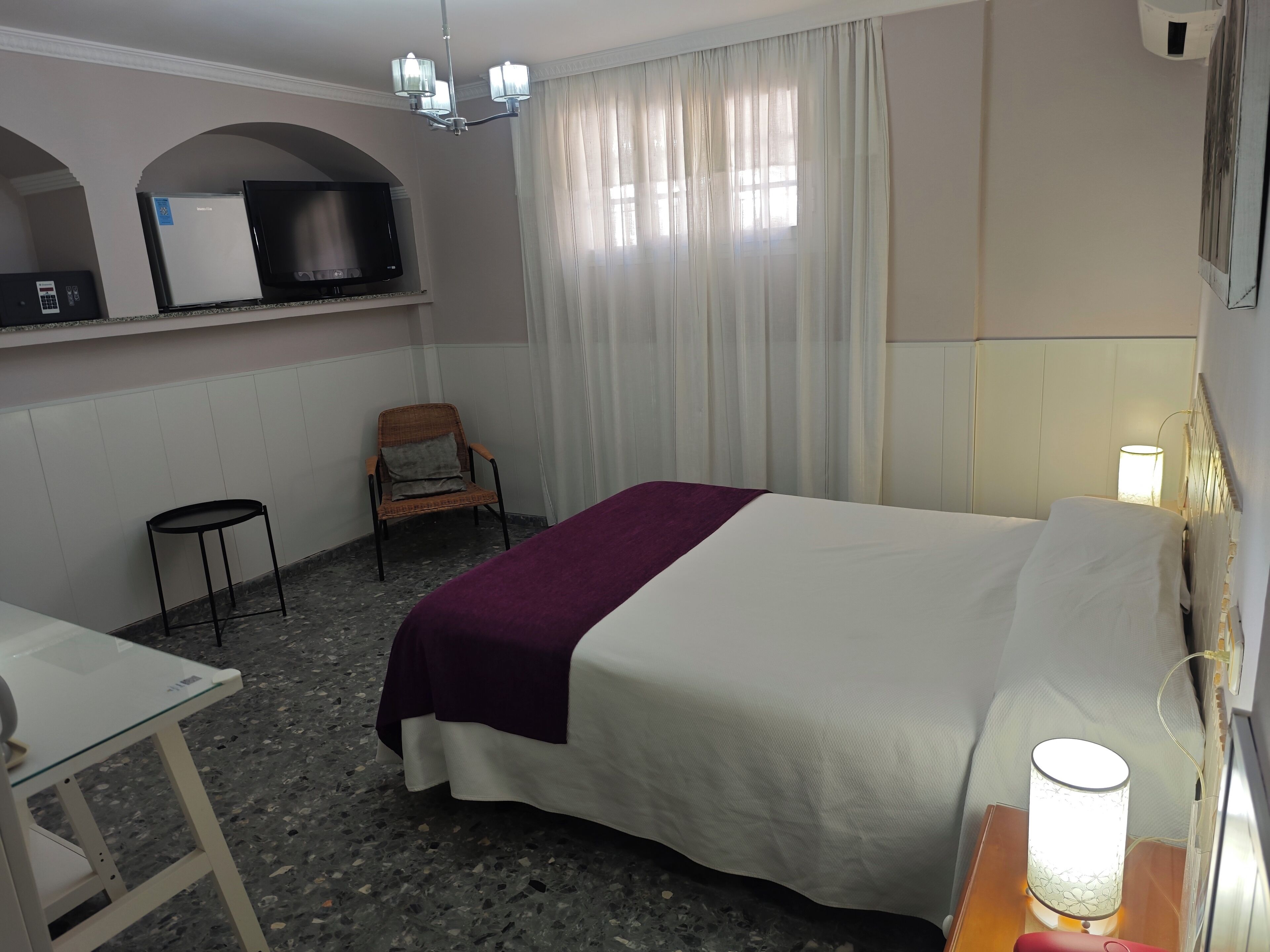 Et hotelværelse med en seng, en stol, et lille bord, et fjernsyn og en lampe.