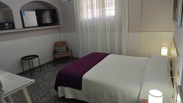 A hotel room with a bed, a chair, a small table, a TV, and a lamp.