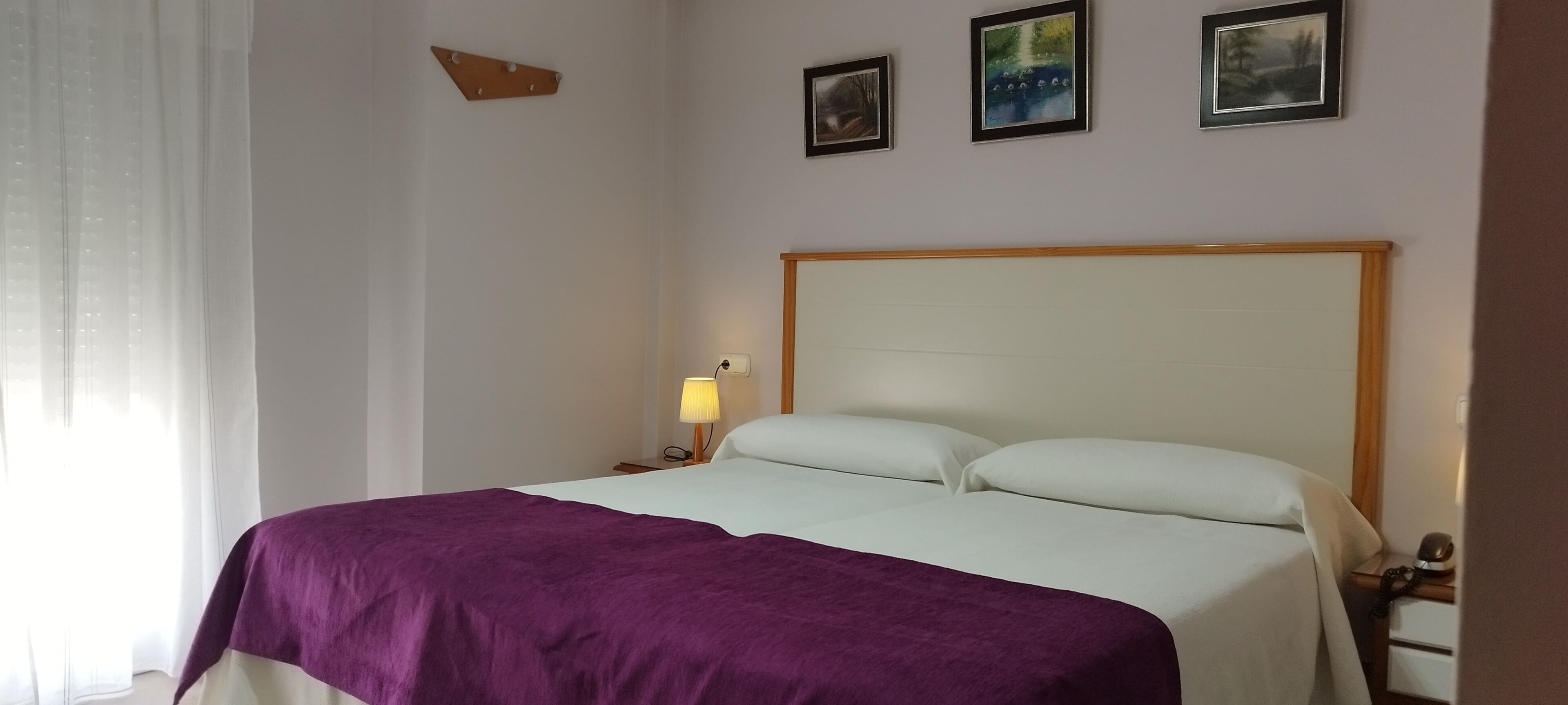 Une chambre d’hôtel avec un lit, une table de chevet avec une lampe et trois tableaux encadrés accrochés au mur.