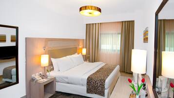 Une chambre d’hôtel avec un lit, des lampes de chevet, une table de chevet avec un téléphone, un miroir et une fenêtre avec des rideaux.