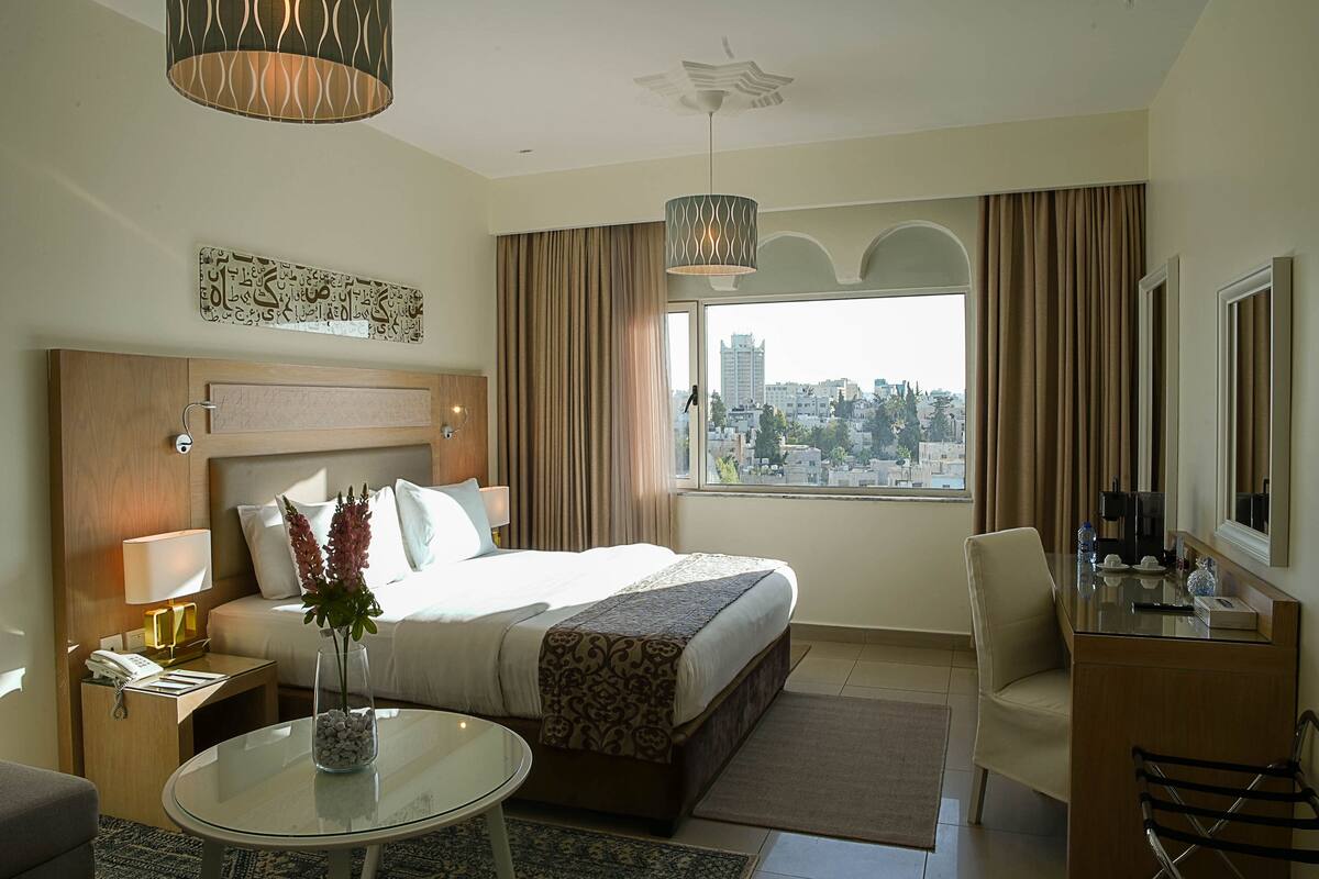 Een hotelkamer met een bed, een bureau, een stoel, een glazen tafel en uitzicht op de stad.