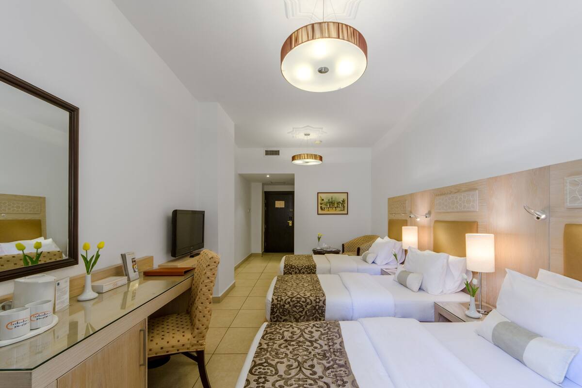 Een hotelkamer met een glazen bureau, twee bedden, een televisie en een grote spiegel.