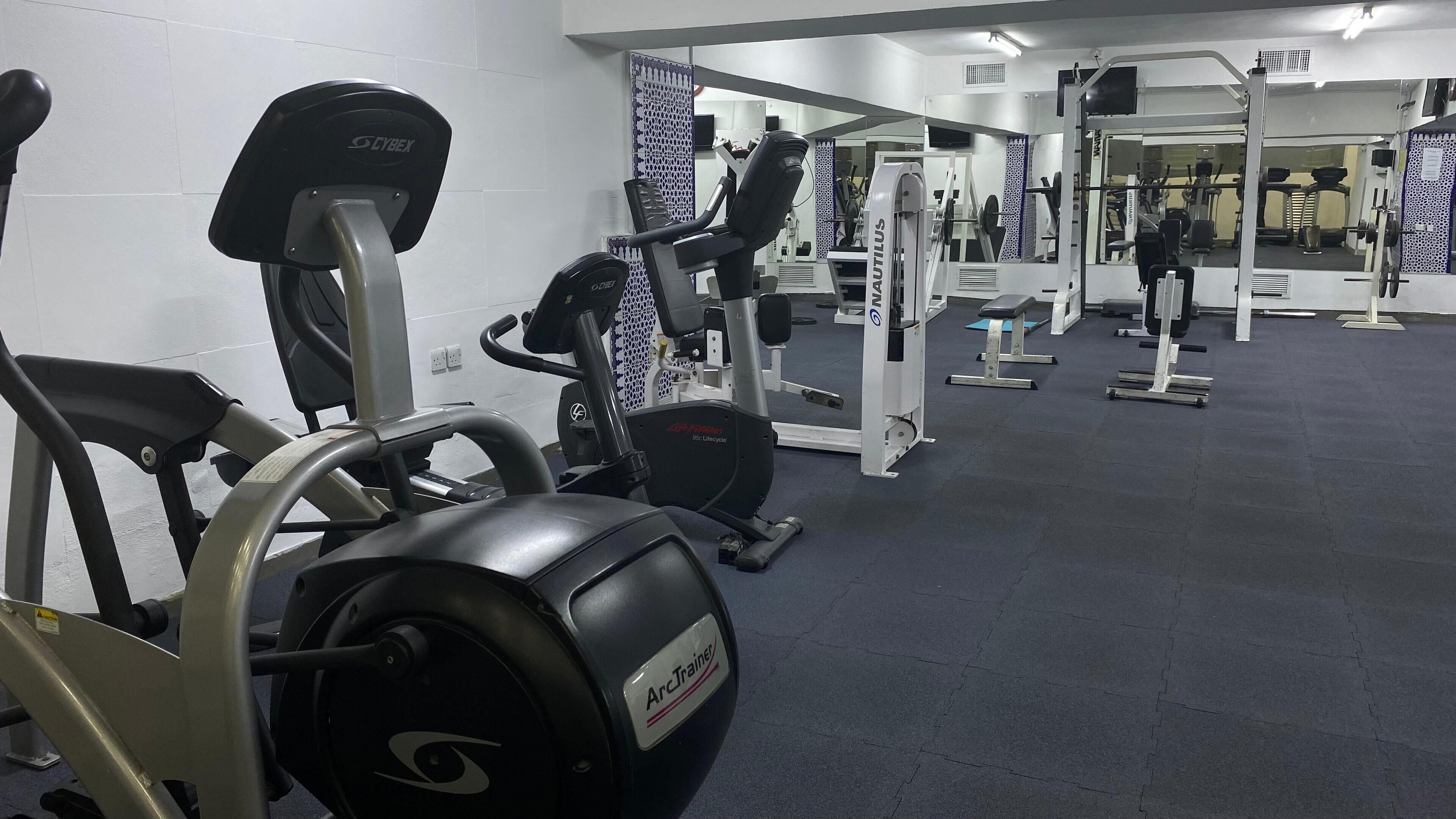 A gym with cardio machines, weightlifting equipment, and a mirrored wall.