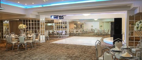 Un amplio salón de banquetes con alfombra estampada, mesas redondas con sillas y una pista de baile central.