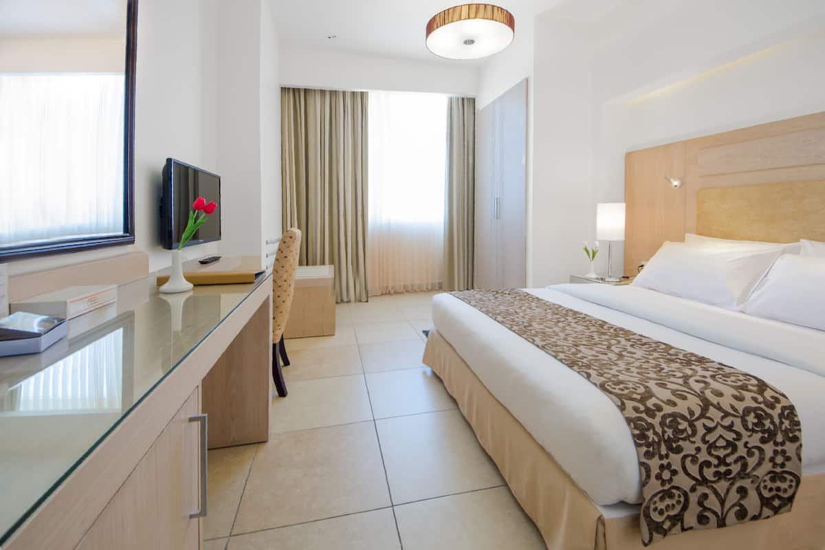 Een hotelkamer met een bed, een bureau met een computer, een televisie en een raam met gordijnen.