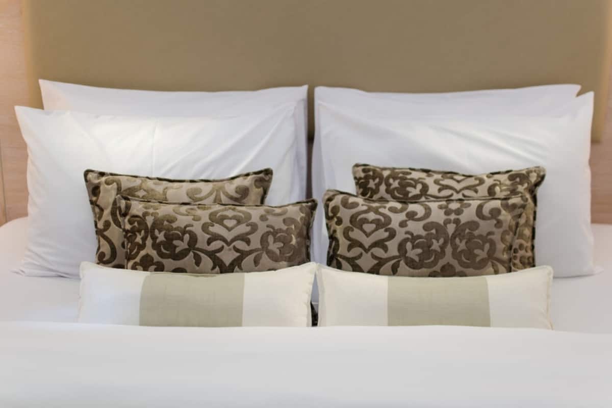 Een bed met witte en gemêleerde kussens, een beige hoofdbord en een lichtkleurige spreidekker.