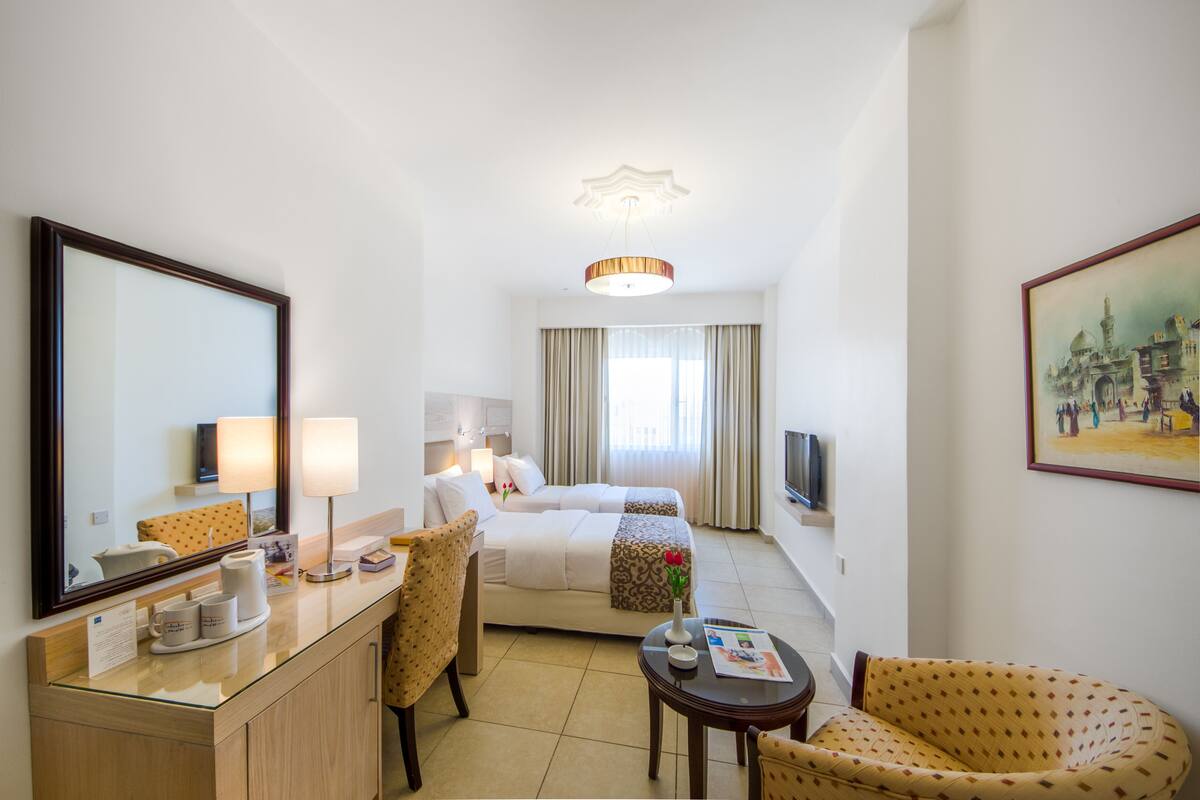 Hotelkamer met een bed, een bureau met spiegel, een stoel, een klein tafeltje en een televisie.