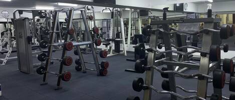 A gym with various weightlifting equipment, including dumbbells and weight plates, and a clock on the wall.
