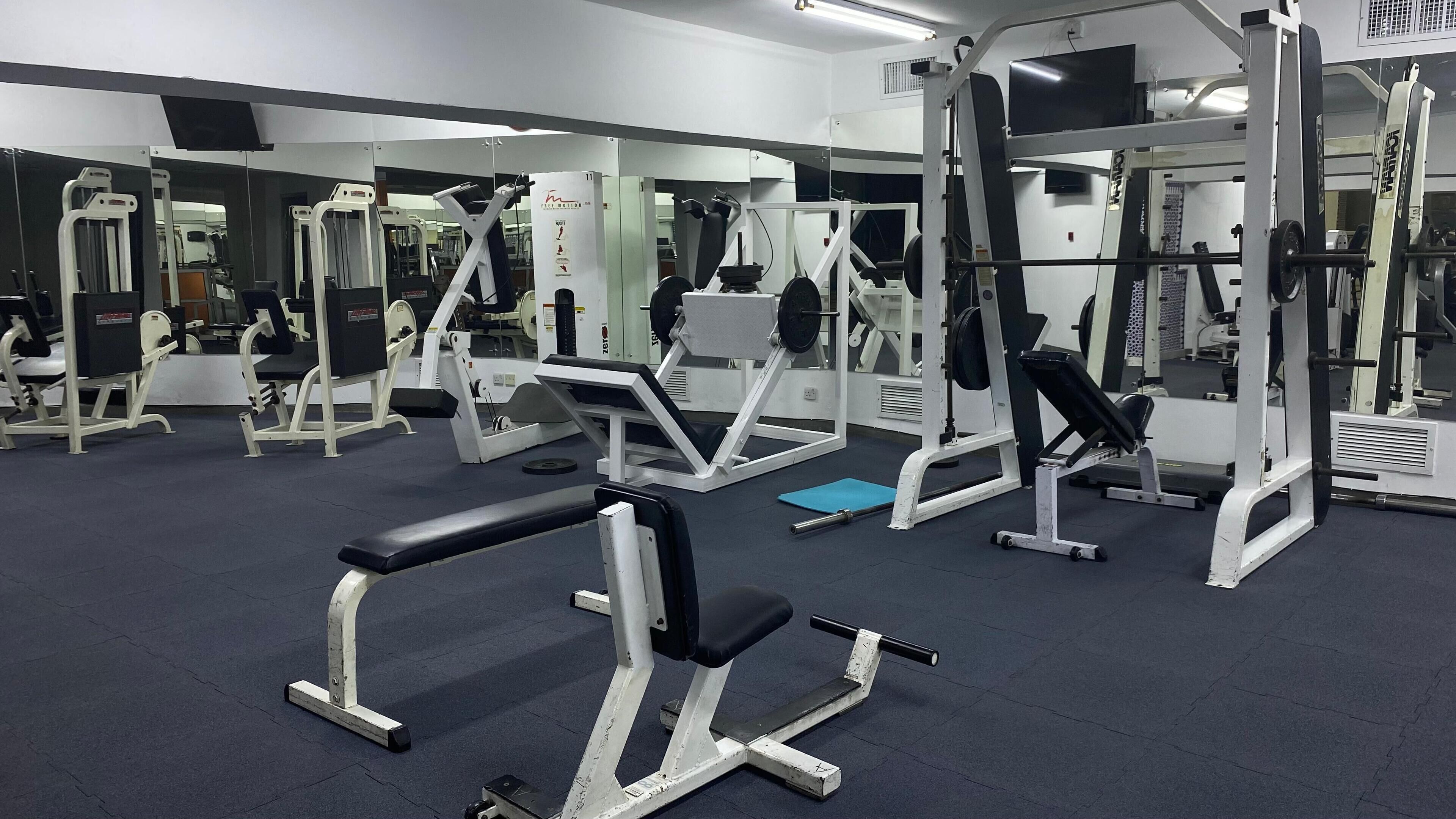 Ein Fitnessstudio mit verschiedenen Trainingsgeräten, darunter Kraftgeräte, Bänke und Kurzhanteln.