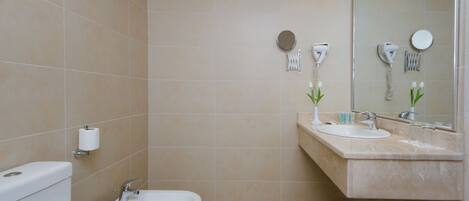 A bathroom with a toilet, bidet, sink, and mirror.