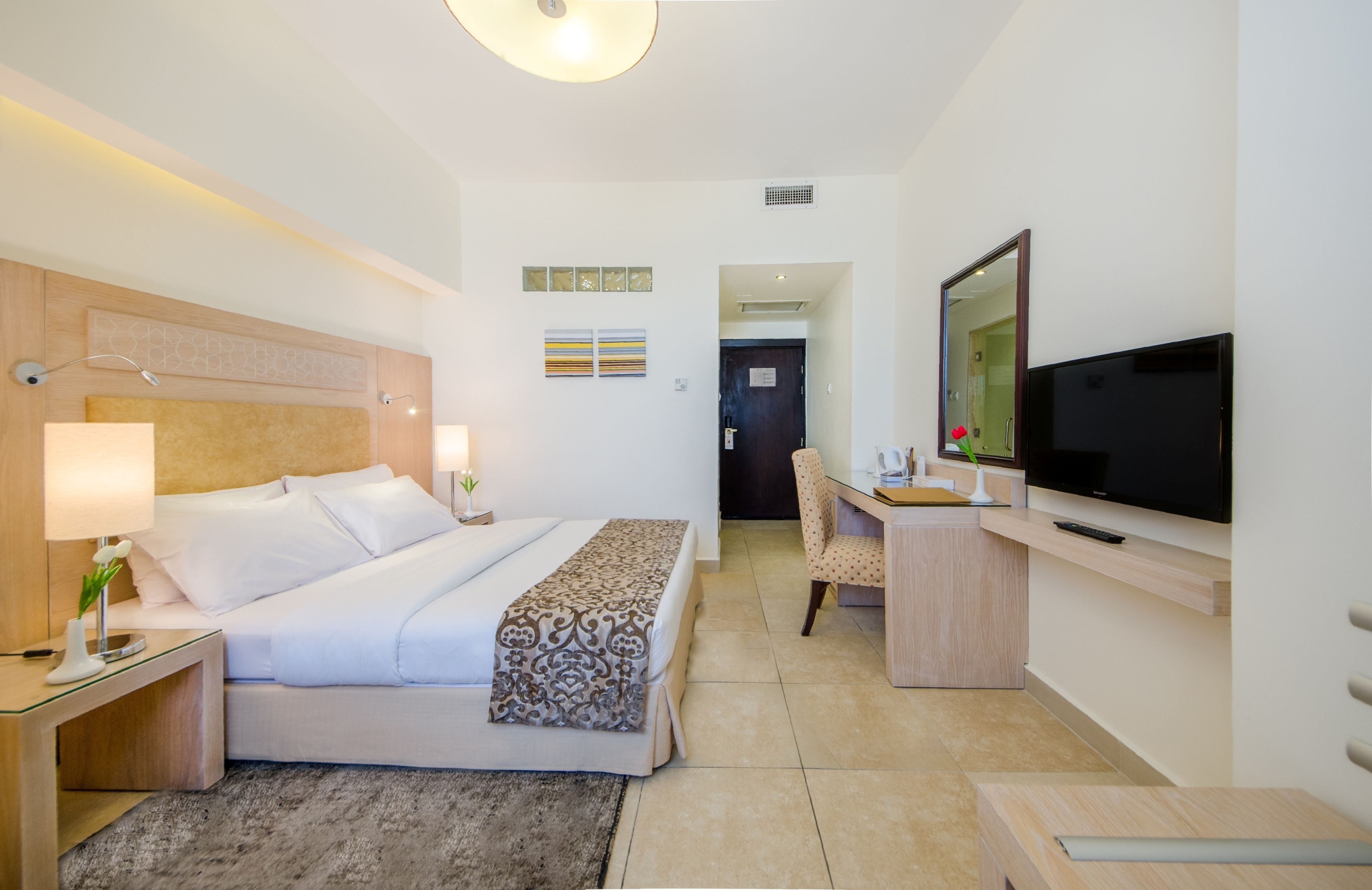 A hotel room with a bed, bedside lamps, a desk with a TV, and a chair.