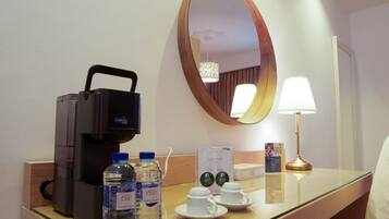 A hotel room with a coffee maker, two water bottles, two cups, a mirror, and a lamp on the counter.