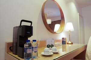 A hotel room with a coffee maker, two water bottles, two cups, a mirror, and a lamp on the counter.