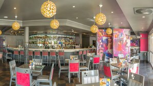 Un restaurant doté d’un bar, de tables avec des coussins rouges et de luminaires sphériques suspendus.