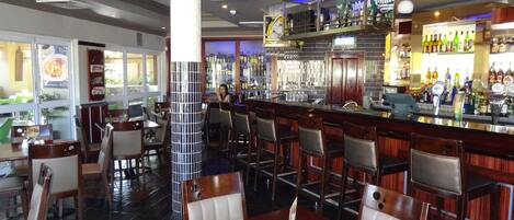 A restaurant with a bar area, wooden tables and chairs, and a tiled floor.