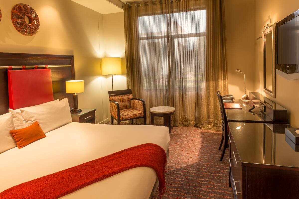 Une chambre d’hôtel avec un lit, un bureau, une chaise, une télévision et une fenêtre avec des rideaux.