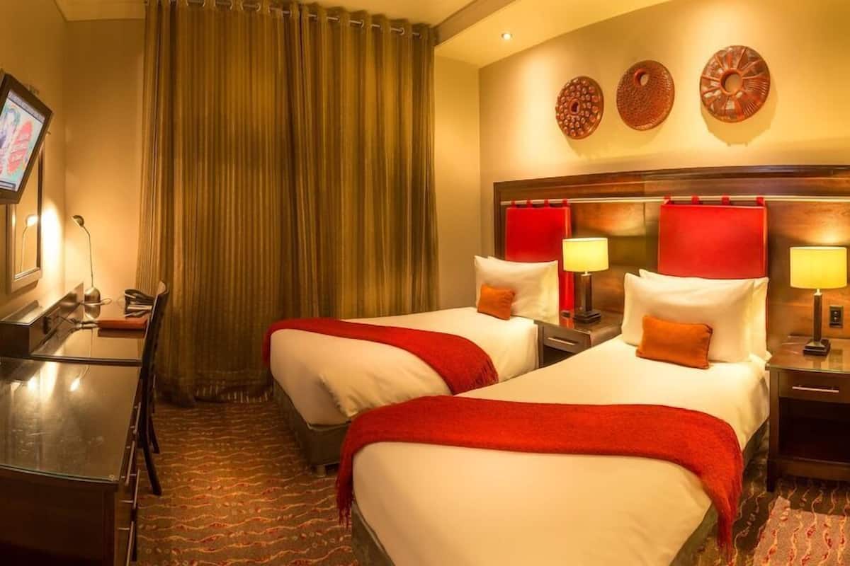 Une chambre d’hôtel avec deux lits, un bureau, une télévision et un rideau rouge.
