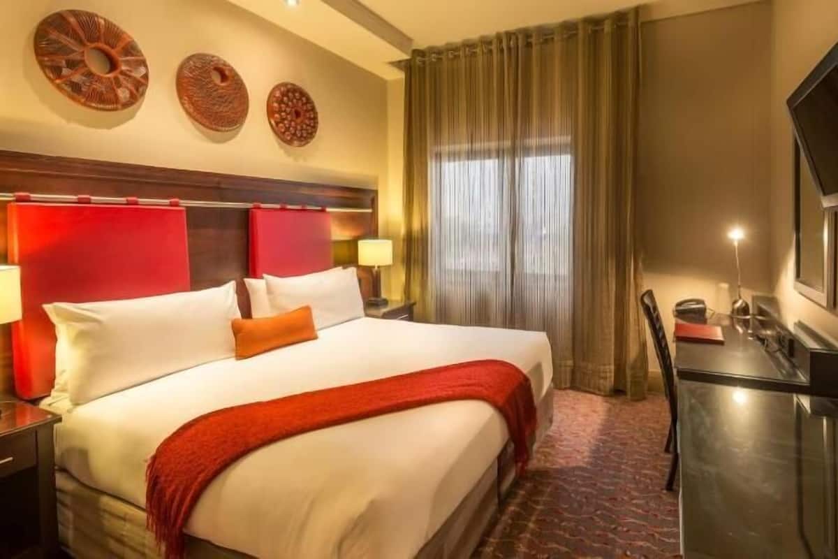 Une chambre d’hôtel avec un lit, un bureau, une télévision et une fenêtre avec des rideaux.