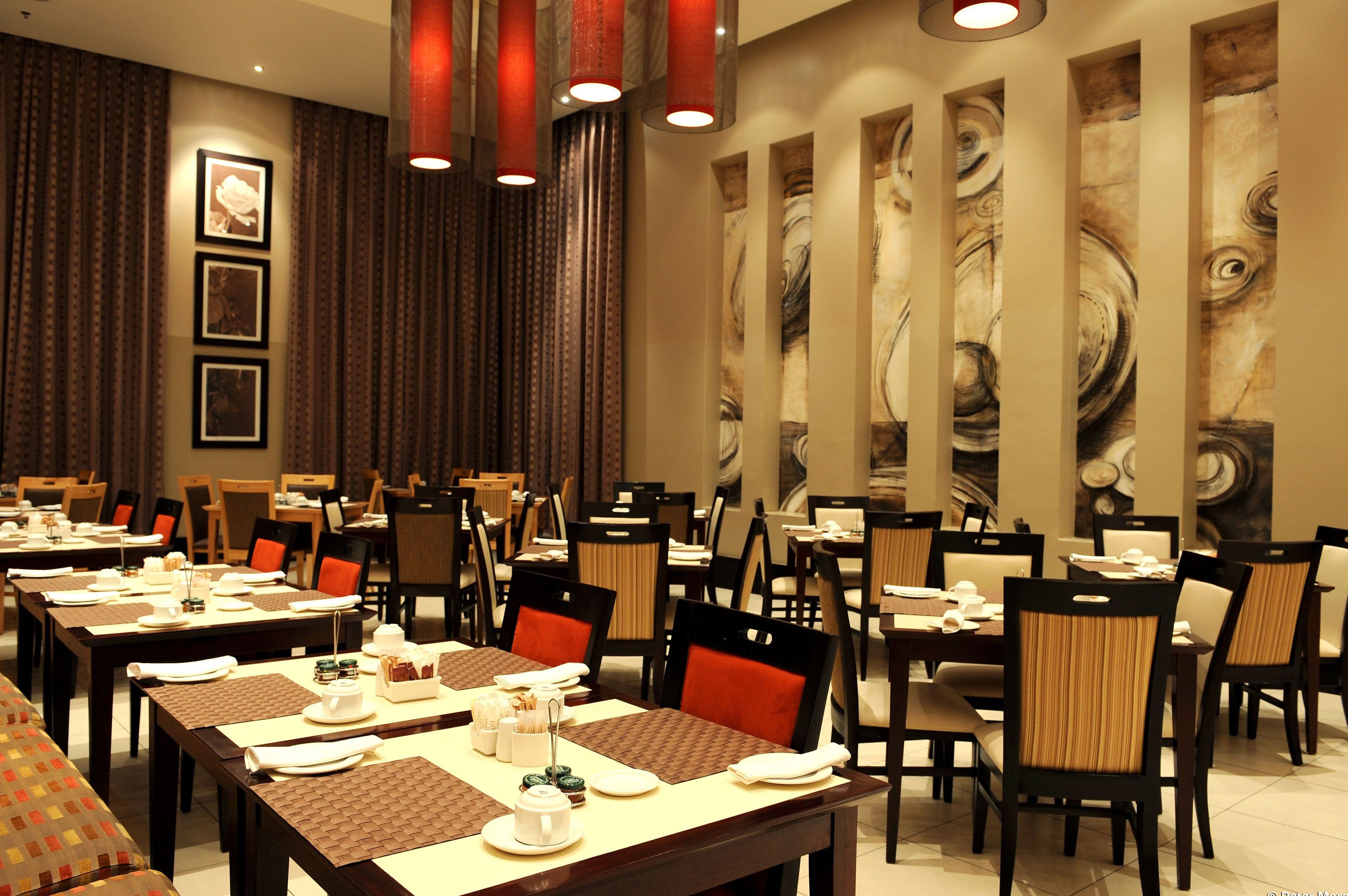 Un comedor de hotel con varias mesas dispuestas para el servicio, sillas y un gran mural abstracto en la pared.