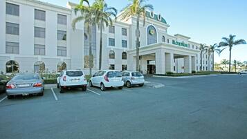 A hotel with a white facade, palm trees, and a parking lot with several cars.
