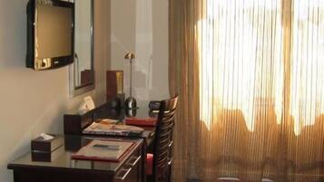 A hotel room with a desk, chairs, a television, and a large window with curtains.