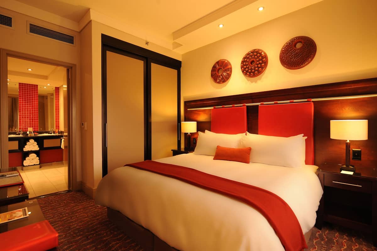 Une chambre d’hôtel avec un grand lit, deux tables de chevet avec des lampes, un plaid rouge et vue sur la salle de bain.