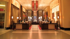 Eine Hotelhalle mit einer zentralen Rezeption, verschiedenen Sitzbereichen und einem roten Teppich zum Eingang.