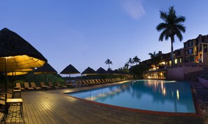 A pool area with lounge chairs and umbrellas, surrounded by palm trees and a building with balconies. - San Lameer Hotel and Spa (Southbroom)