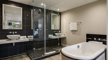 A modern bathroom with a large bathtub, a glass-enclosed shower, and two sinks with mirrors.