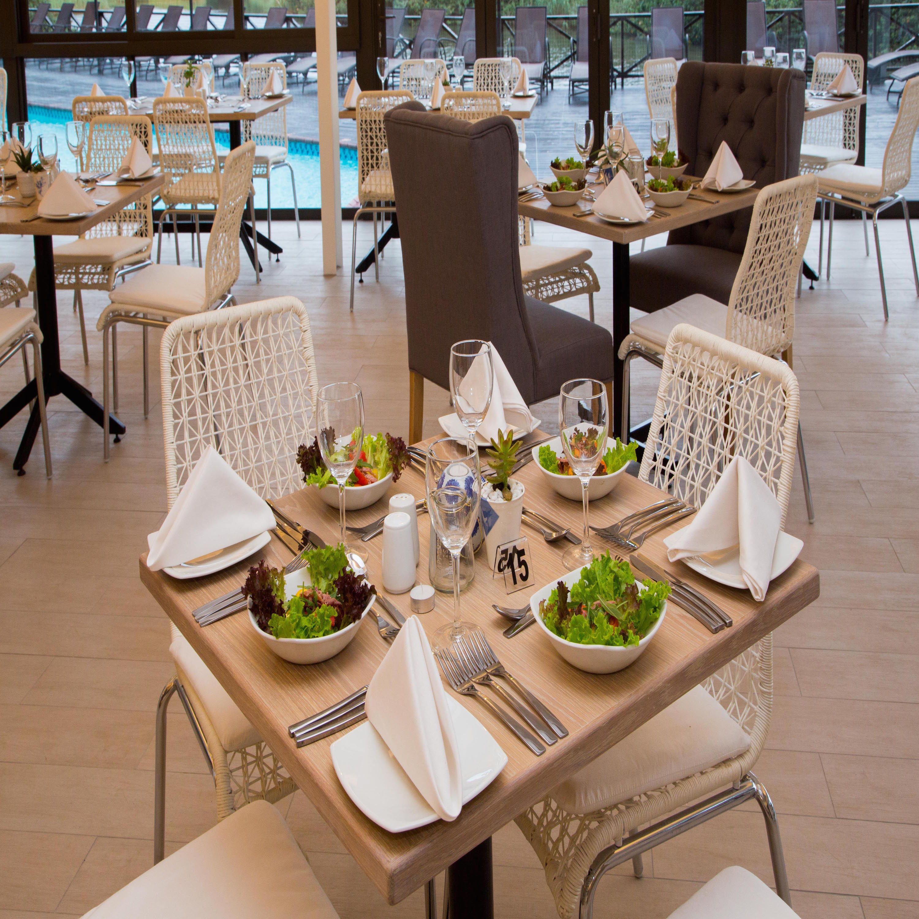 A restaurant setting with tables set for dining, chairs, and a view of the outdoor area.