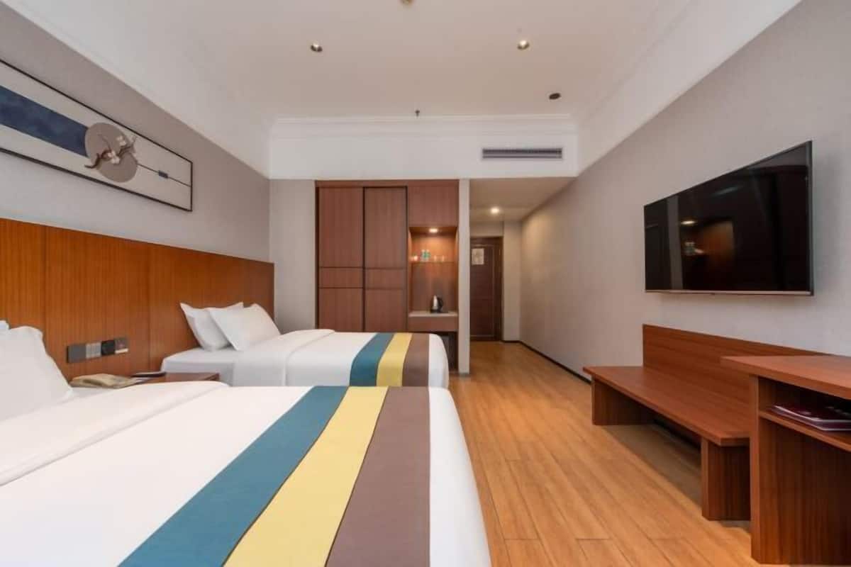 A hotel room with two beds, a TV, wooden furniture, and a hallway leading to another room.
