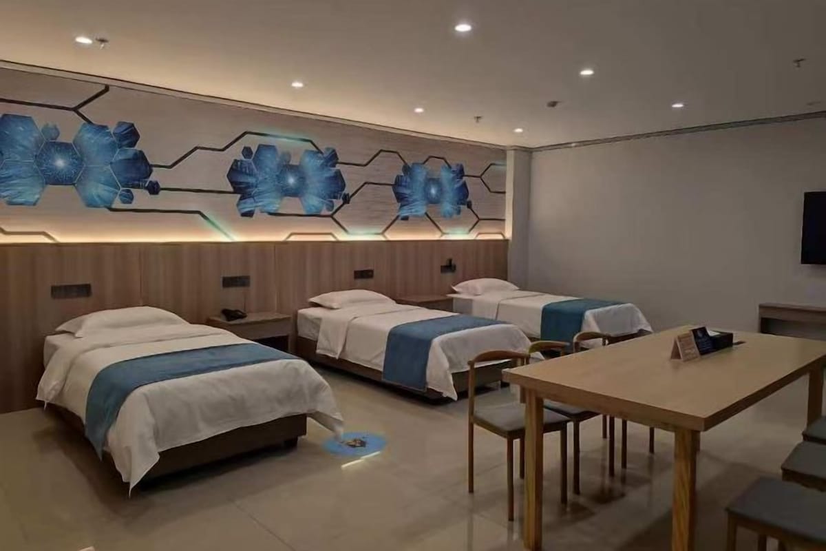 A hotel room with three beds, a wooden table, and a wall-mounted artwork.